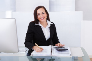 27864859 - portrait of happy businesswoman calculating tax at desk in office
